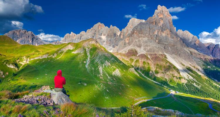 Persona con chaqueta roja disfrutando de una vista panorámica de montañas escarpadas.