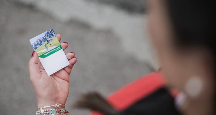 Primer plano de una mano sosteniendo una tarjeta de pase turístico con imágenes alpinas, superficie de la carretera desenfocada en el fondo.