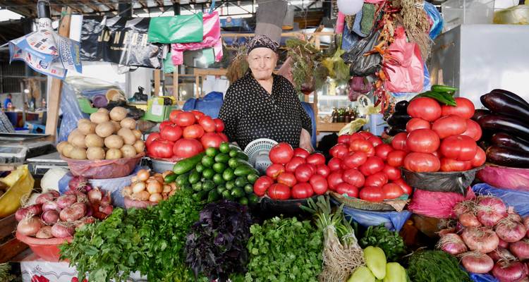 Verkoper bij een marktkraam met verschillende groenten en fruit.