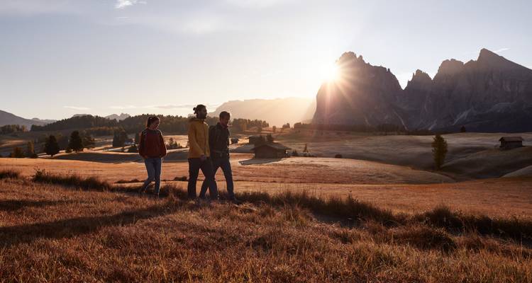 Drie mensen die lopen bij zonsondergang met bergen op de achtergrond.