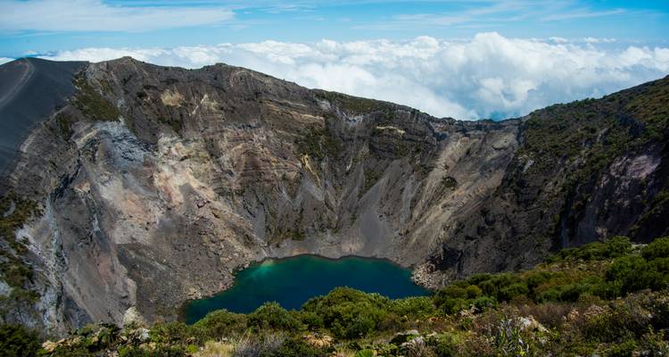 Cratère volcanique avec un petit lac à l'intérieur, entouré de nuages.