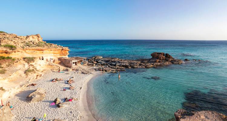 Crique de sable avec des gens qui prennent le soleil et nagent dans l'eau turquoise.