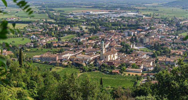 Vista elevada de un pueblo italiano rodeado de viñedos, campos e industria distante.