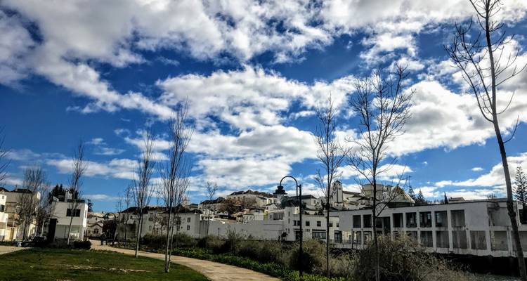 Bâtiments blancs modernes et ville perchée sur une colline lointaine sous un ciel rempli de nuages dramatiques.