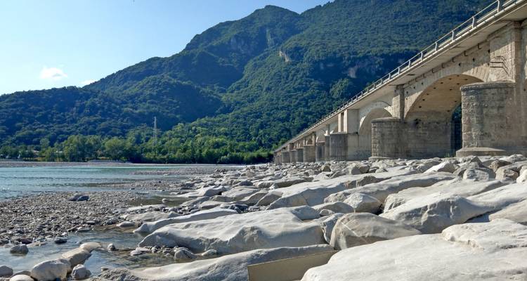 Eine Steinbrücke über einen Fluss mit einem Berg im Hintergrund.