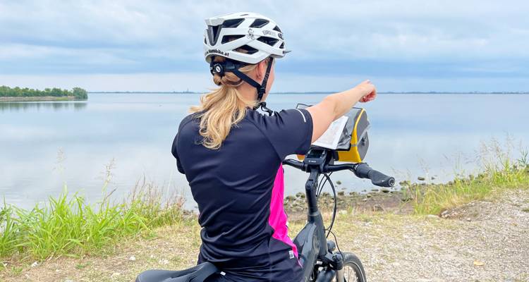 Eine Frau auf einem Fahrrad zeigt über eine Uferpromenade.