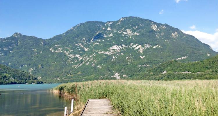 Ein Holzsteg, der zu einem See mit Bergkulisse führt.