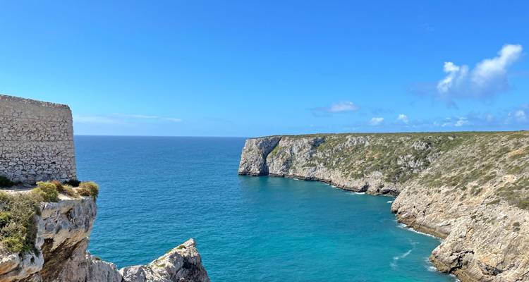 Acantilados empinados de piedra caliza rodeando una cala turquesa del Atlántico bajo un cielo claro de verano.