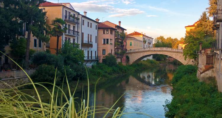 Stone bridge arches over calm canal flanked by colourful historic townhouses at sunset.