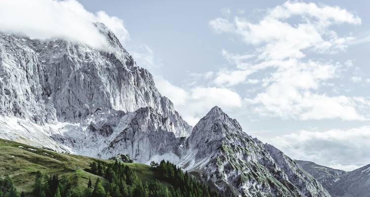Pics rocheux de montagne avec une végétation luxuriante et des nuages.