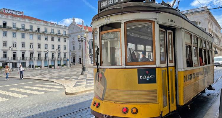 Ikonische gelbe Straßenbahn gleitet durch einen historischen Lissaboner Platz mit gemustertem Pflaster und weißen Fassaden.