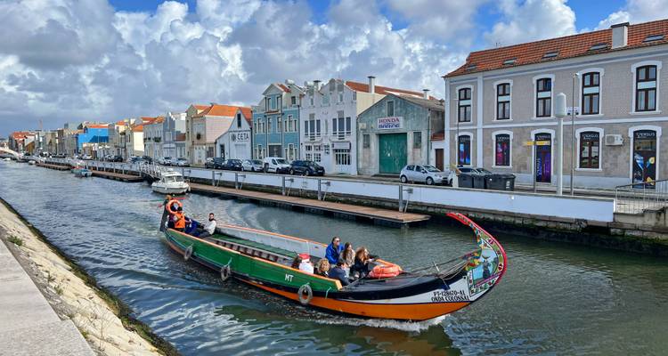 Buntes Moliceiro-Boot von Aveiro fährt entlang des Kanals an pastellfarbenen Ufergebäuden vorbei.