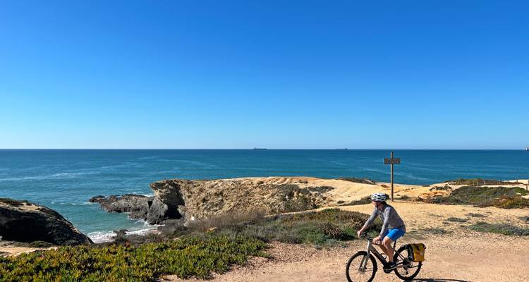 Radfahrer fährt entlang eines zerklüfteten Klippenwegs mit Blick auf den tiefblauen Atlantik.