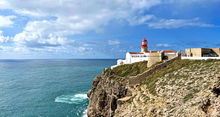 Der rot bekrönte Leuchtturm von Cabo de São Vicente thront dramatisch auf einer hohen Meeresklippe.