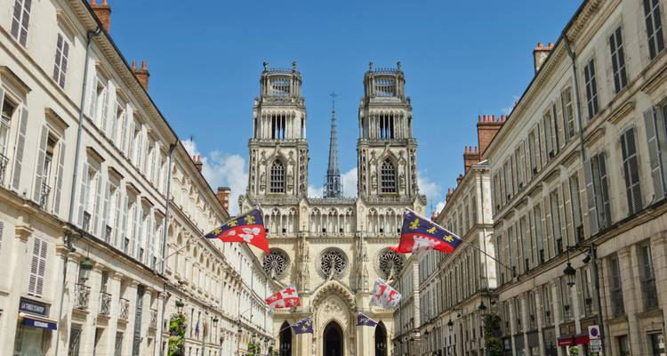 Vue de face d'une grande cathédrale avec des drapeaux et un ciel bleu dégagé.