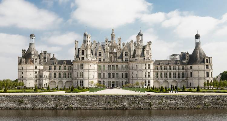 Château de Chambord avec un canal devant et des gens qui se promènent à proximité.