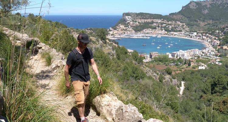Hiker walking along a trail overlooking a coastal town and bay.