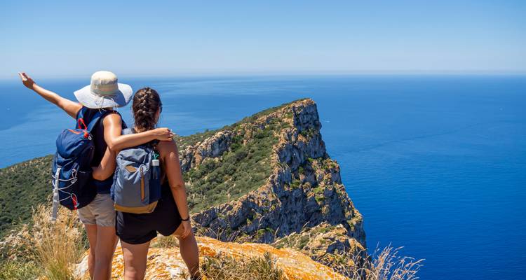 Two hikers on a cliff edge pointing out at a vast ocean view.