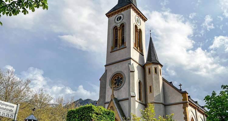 A church tower under a partly cloudy sky, with mountains in the background.