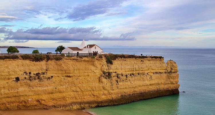 Une chapelle blanche perchée sur une falaise rocheuse au bord de mer.