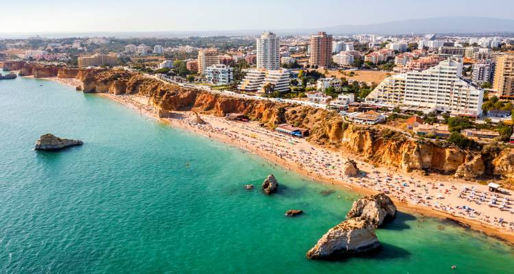 Vista aérea de una playa concurrida con acantilados y horizonte de la ciudad.
