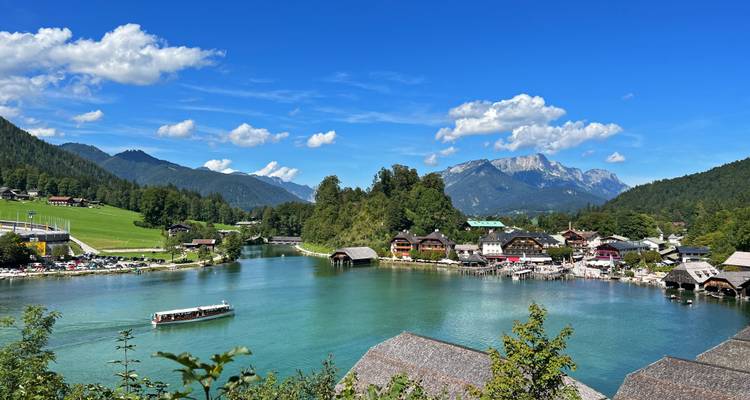 Kristalheldere alpiene meer omringd door chaletchaletdorp en dramatische Beierse bergtoppen onder een levendige blauwe hemel.
