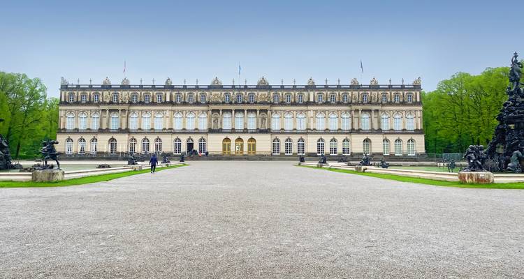 Symmetrisch frontaal zicht op Schloss Herrenchiemsee met brede grindvoorplein en naderende bezoekers.