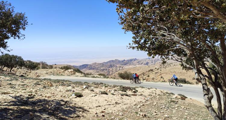 Deux cyclistes sur une route dans un paysage rocheux et vallonné avec des arbres.