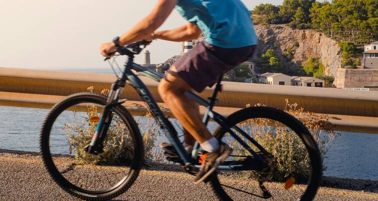 Un cycliste sur une route côtière avec un phare en arrière-plan.