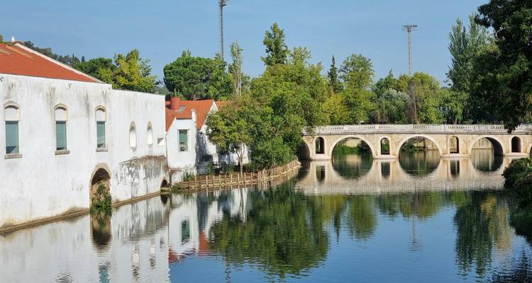 Buildings reflecting on a calm river near an old stone bridge.