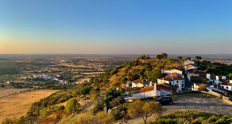 Vue panoramique d'un village à flanc de colline avec des champs étendus.