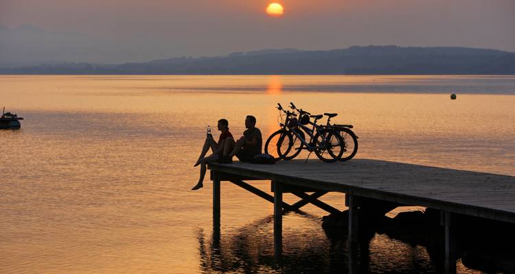 Couple assis sur un quai pendant le coucher du soleil au bord d'un lac.