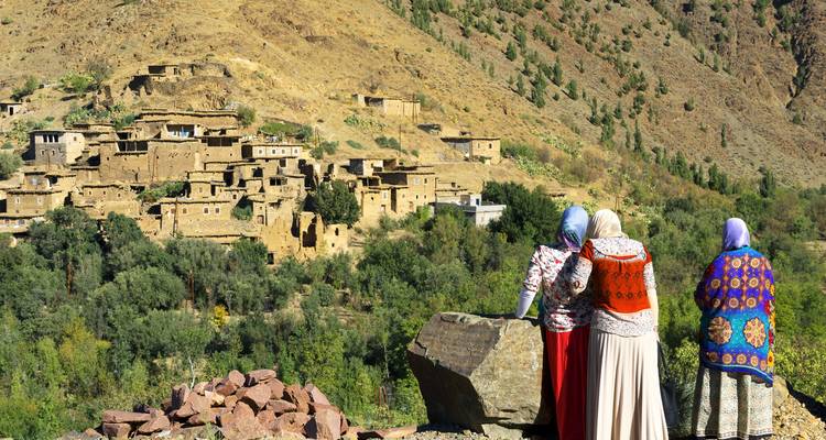Drei traditionell gekleidete Frauen blicken auf ein Bergdorf hinab.