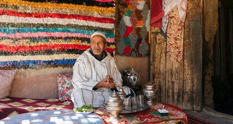 Mann sitzt in einem traditionell dekorierten Geschäft mit bunten Textilien.