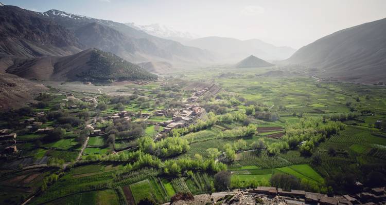 Weites grünes Tal mit kleinen Dörfern und felsigen Bergen.