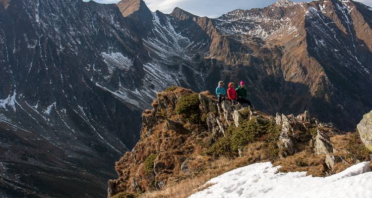 Trois personnes assises au sommet d'une montagne rocheuse avec des plaques de neige.