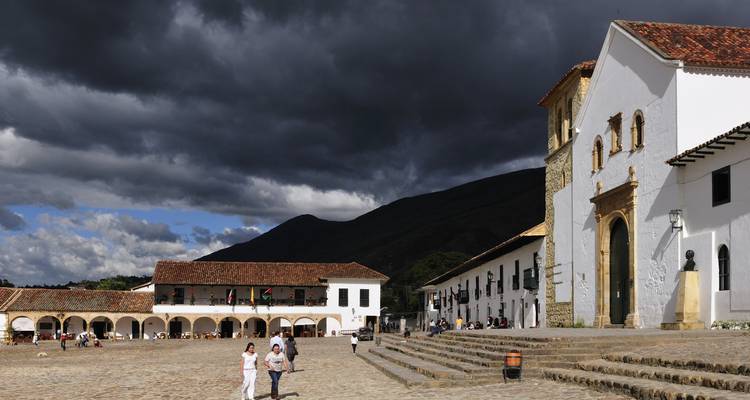 Platz im Kolonialstil mit gehenden Menschen unter einem dunklen, bewölkten Himmel.