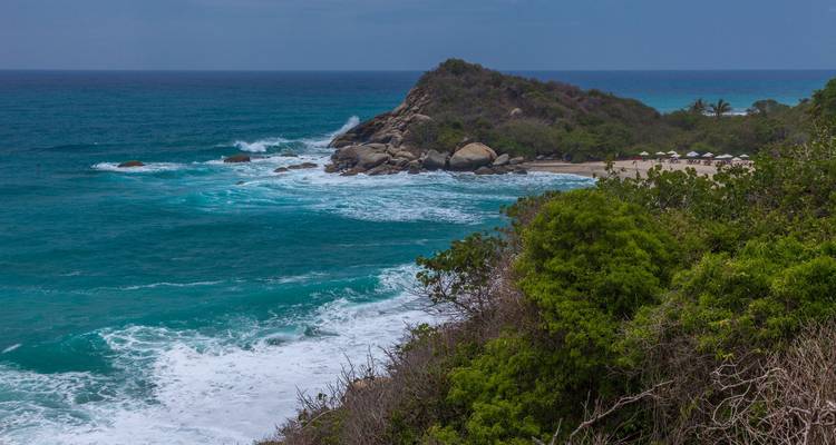 Felsiger Strand mit brechenden Wellen und einem dichten Wald in der Nähe.