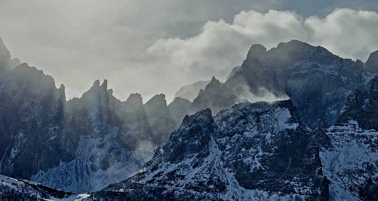 Nuages et lumière du soleil filtrant au-dessus des pics montagneux escarpés