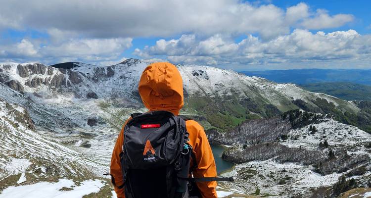 Hiker in an orange jacket overlooking a snowy mountain range.