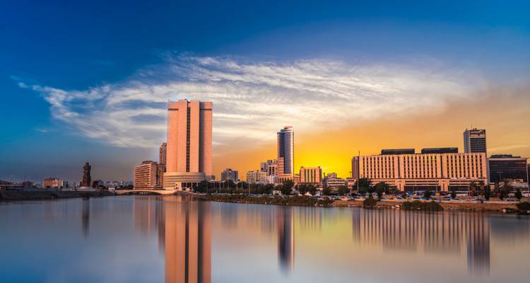 Moderne Stadtsilhouette mit Gebäuden, die sich bei Sonnenuntergang in einem Fluss spiegeln.