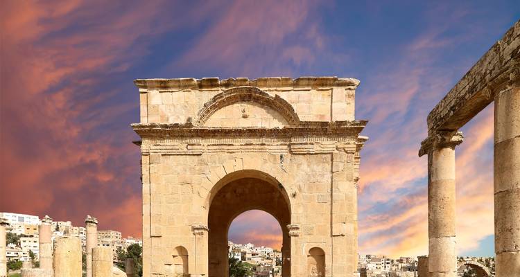 Ancient stone arch of Jerash ruins framed by vibrant sunset clouds.