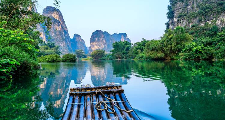 Bamboo raft floating on a river surrounded by limestone cliffs.