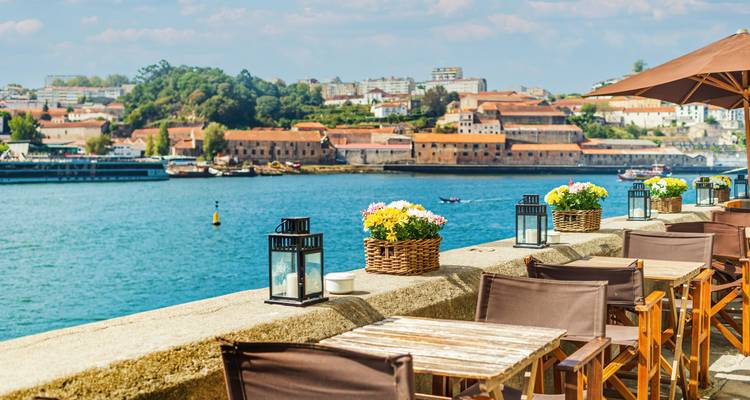 Café en plein air avec des fleurs éclatantes donnant sur une rivière avec vue sur la ville.