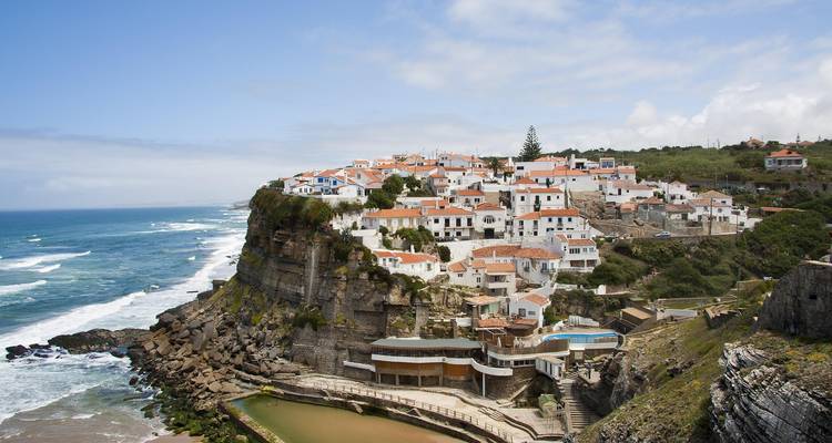 Village côtier perché sur des falaises avec un rivage rocheux et des bâtiments blancs aux toits rouges.