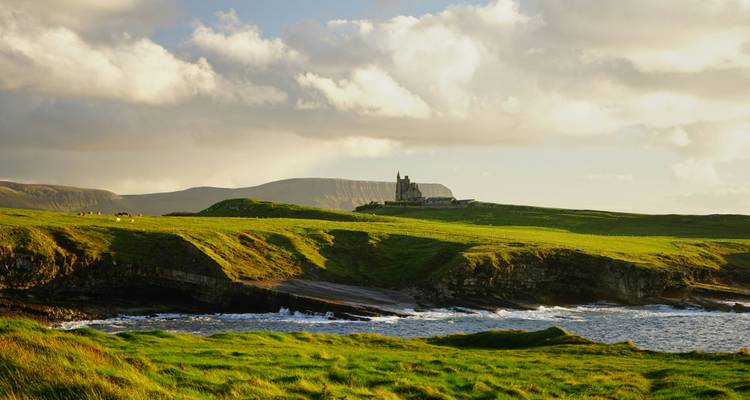 Green rolling hills with a historic building in the background.