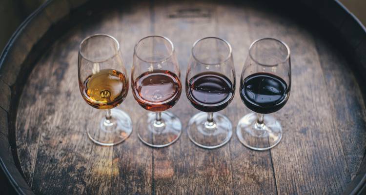 Four glasses of wine on a wooden barrel surface.