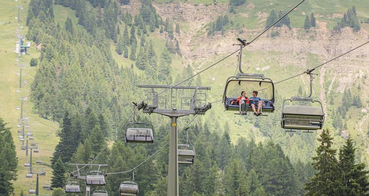 Two persons riding a chairlift over a lush green landscape.