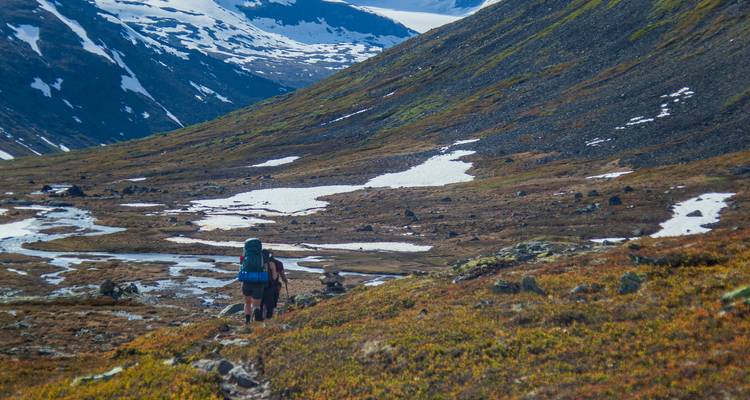 Hikers walking along a rocky mountain trail with snow patches.