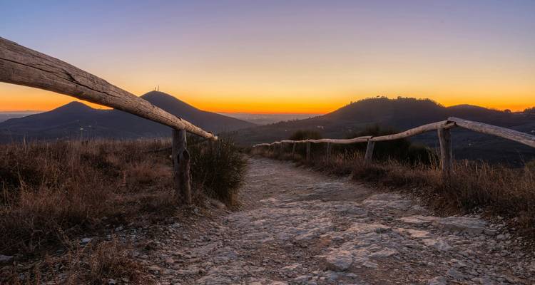 Rustiek landschap met heuvels omlijst door een houten hek tijdens zonsondergang.